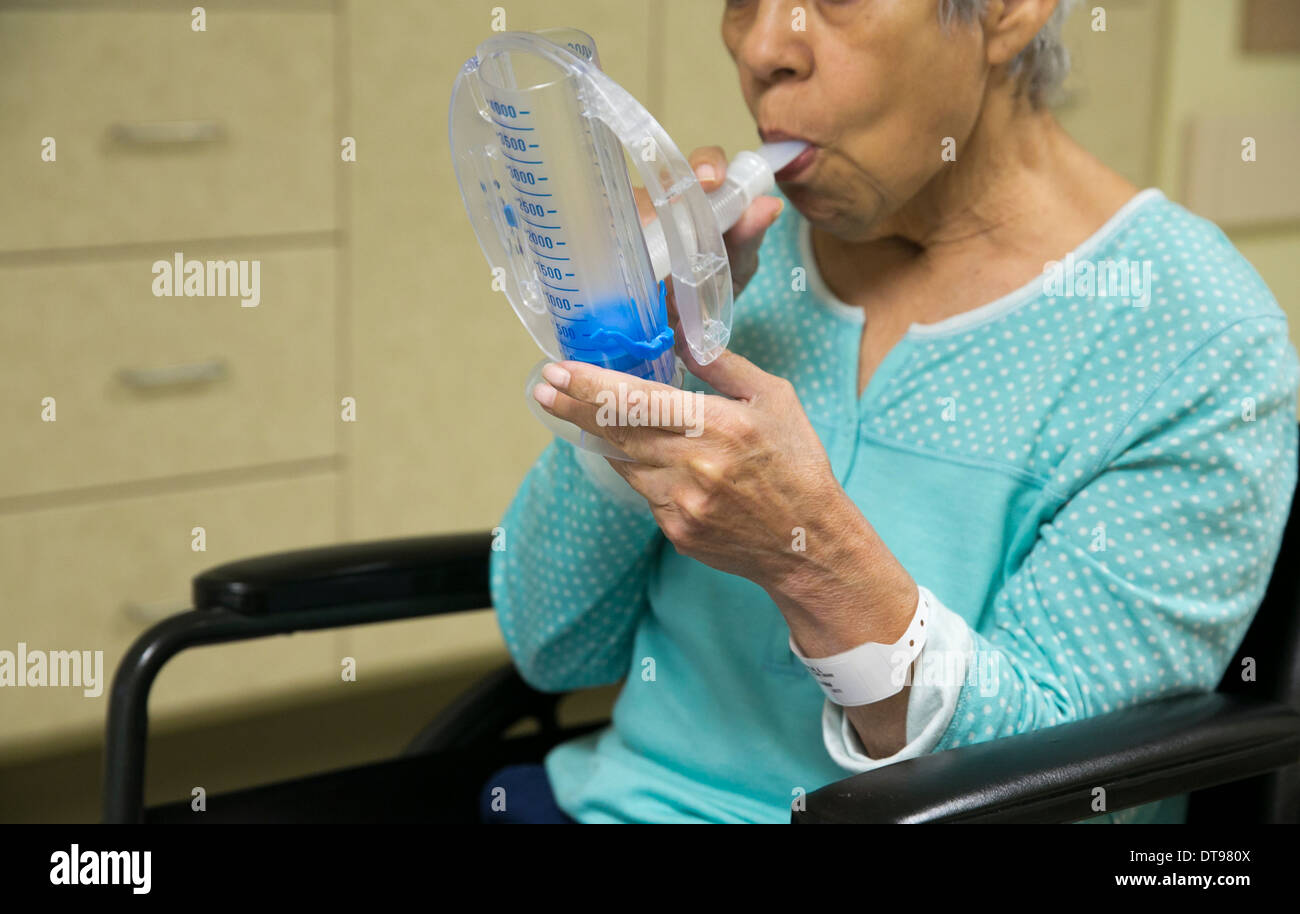 75 year old Hispanic senior citizen uses a medical breathing exercise apparatus while in a rehabilitation hospital in Texas. Stock Photo
