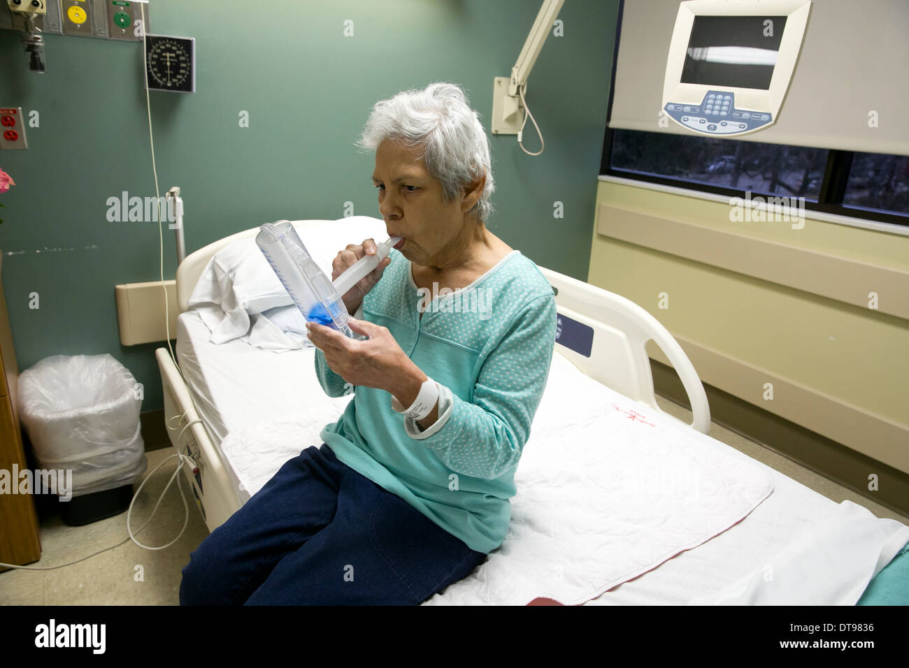 75 year old Hispanic senior citizen uses a medical breathing exercise apparatus while in a rehabilitation hospital in Texas. Stock Photo