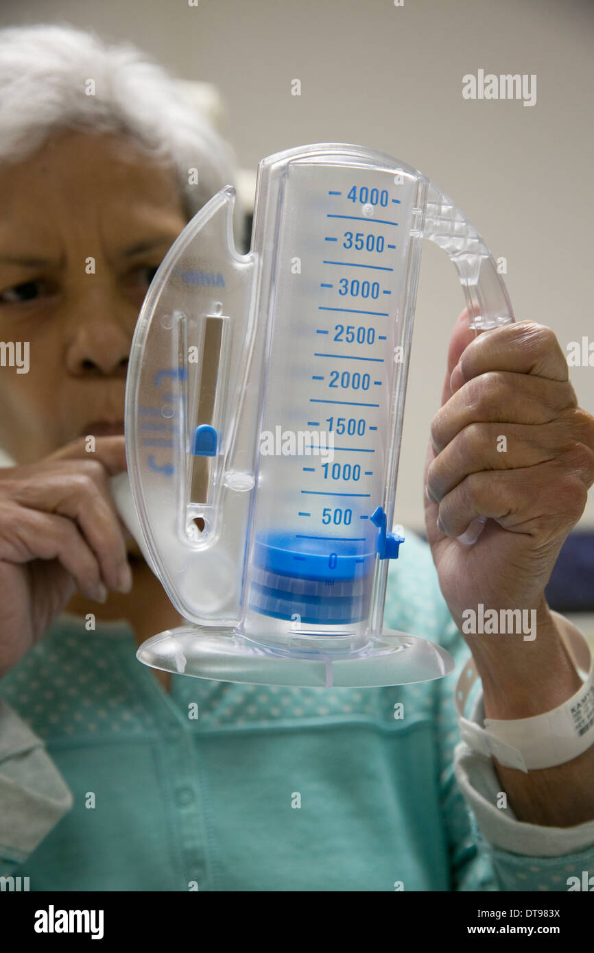 75 year old Hispanic senior citizen uses a medical breathing exercise apparatus while in a rehabilitation hospital in Texas. Stock Photo