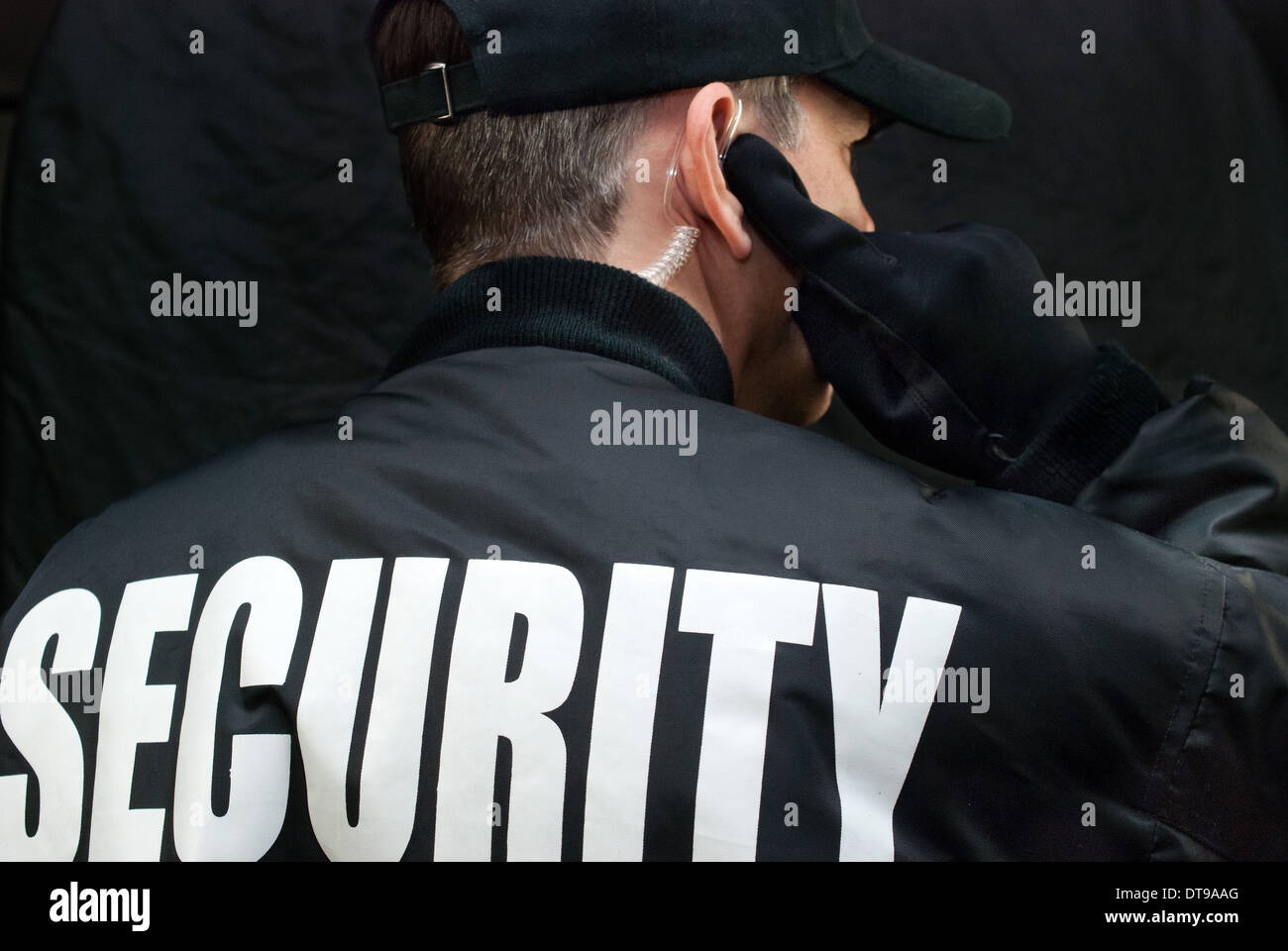 Close-up of a security guard listening to his earpiece. Back of jacket showing. Stock Photo