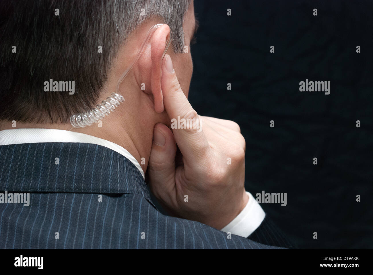 Close-up of a secret service agent listening to his earpiece, over the shoulder. Stock Photo