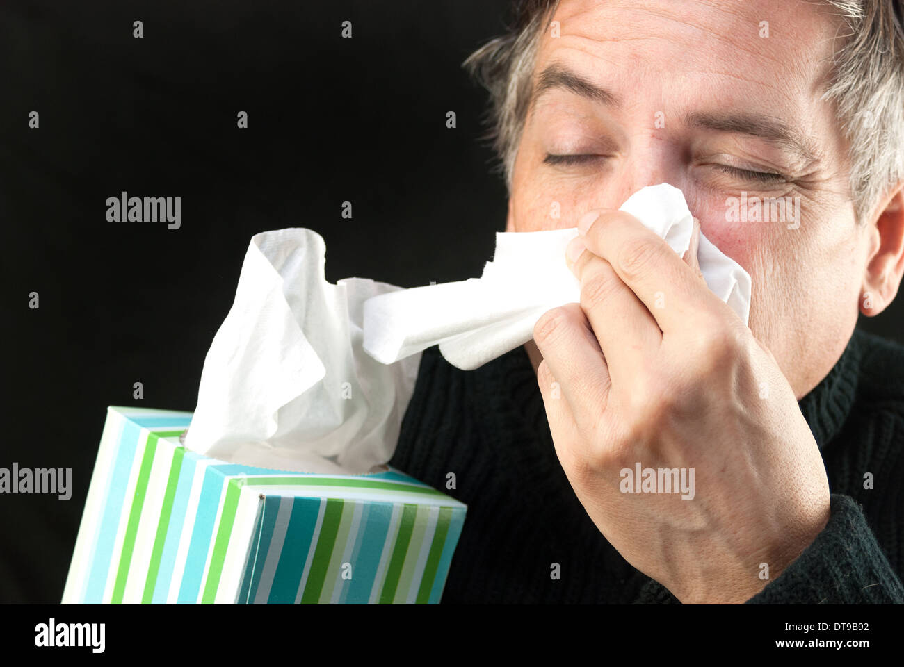 Close-up of a man blowing his nose while holding a tissue box. Stock Photo
