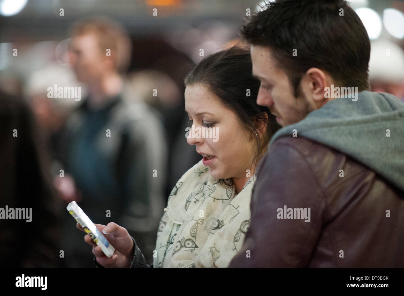 MANCHESTER, UK. 12th February, 2014. A couple check their smartphone for information at Manchester Piccadilly train station during strong winds across the United Kingdom, which led to to travel disruption for evening commuters. Some travellers were advised to postpone their travel plans for the day. Credit:  Russell Hart/Alamy Live News. Stock Photo