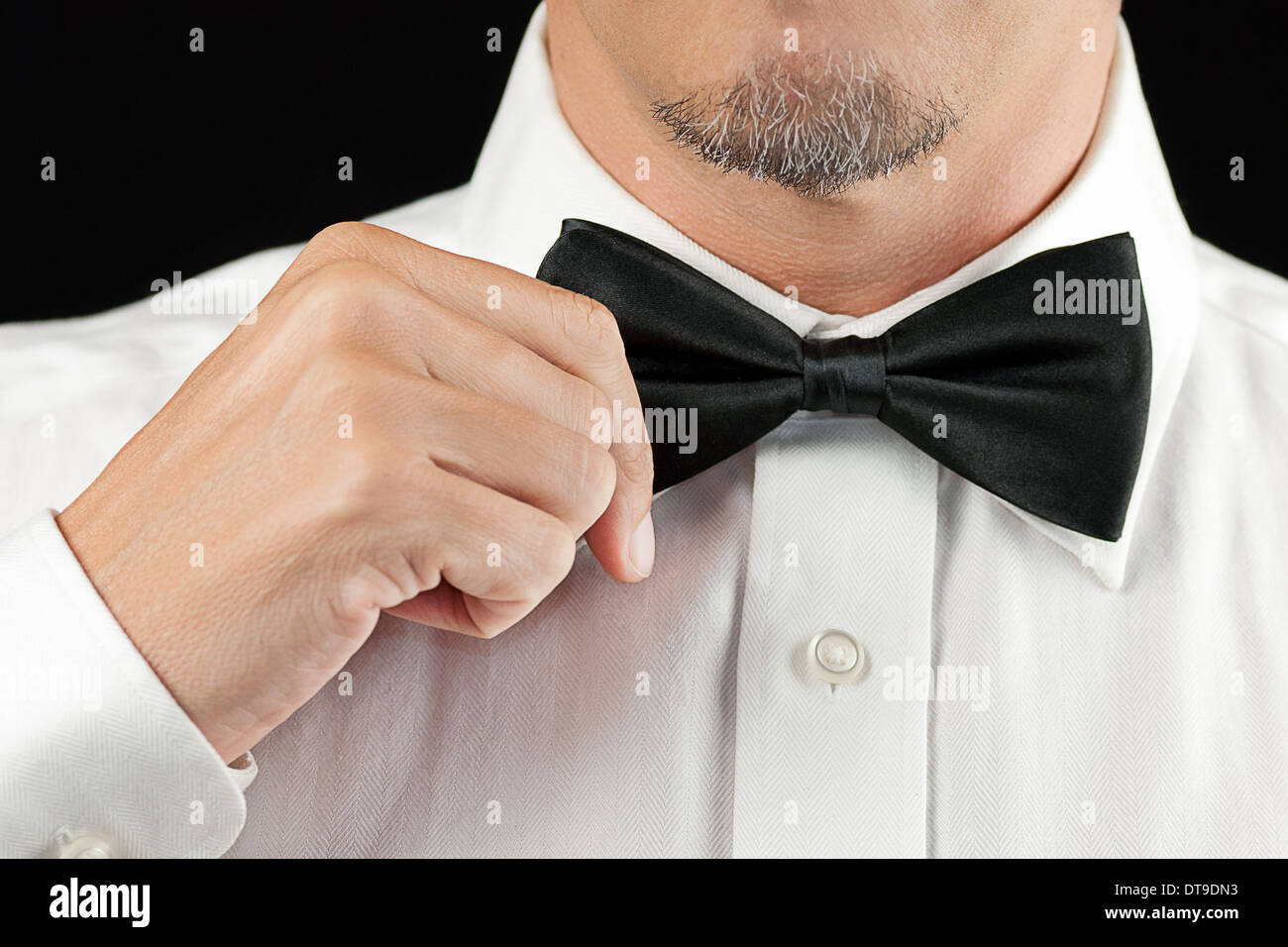 Close-up of a man in a tux straightening his bowtie, one hand, no jacket. Stock Photo