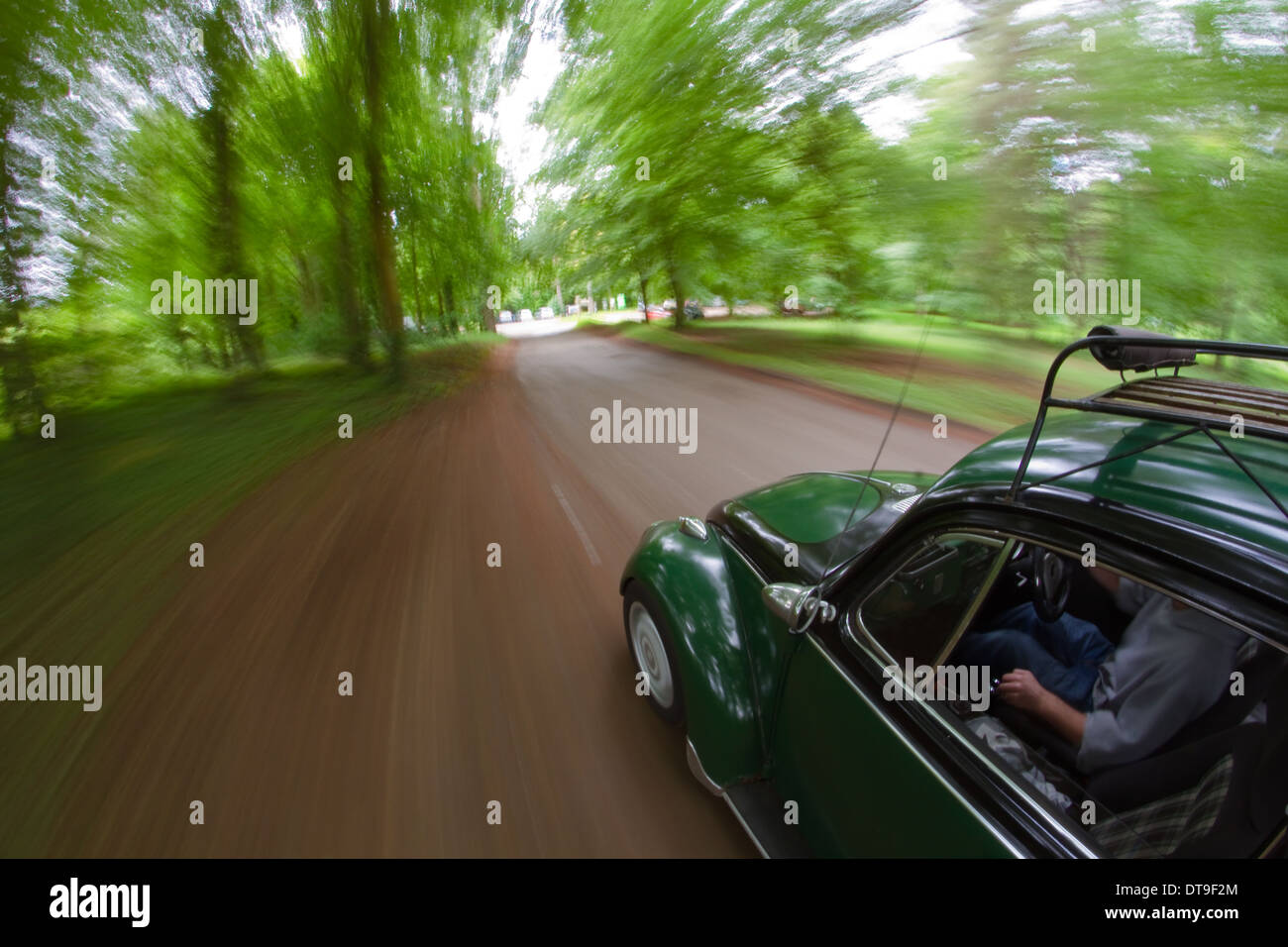 driving in a classic aircooled Volkswagen beetle with a vintage roof rack and two toned paint down a wooded lane. Stock Photo