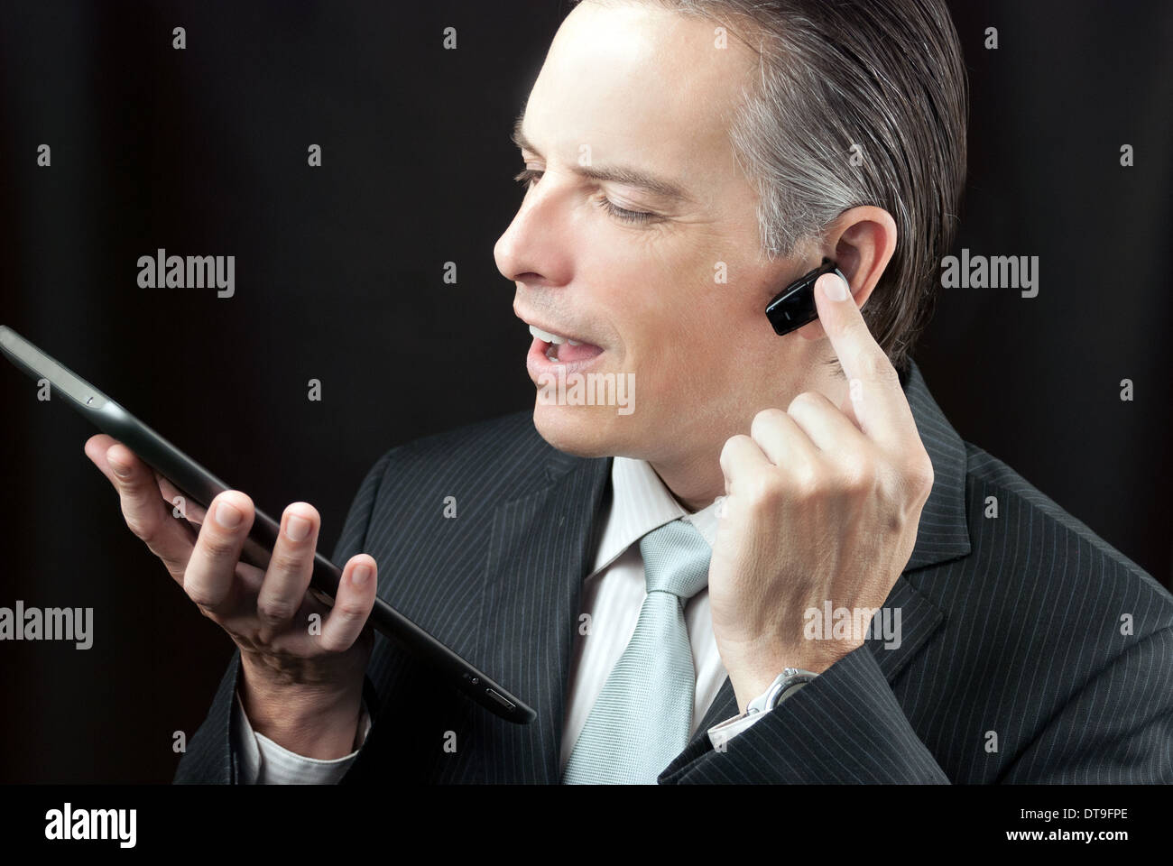 Close-up of a businessman using a tablet adjusting his earpiece headset. Stock Photo
