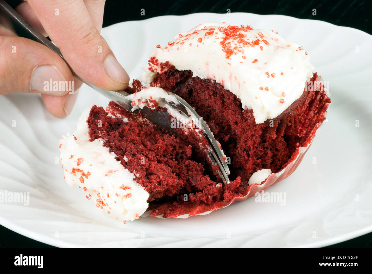 Close-up of a red velvet cupcake on a plate with a man's hand holding a fork slicing into it. Stock Photo