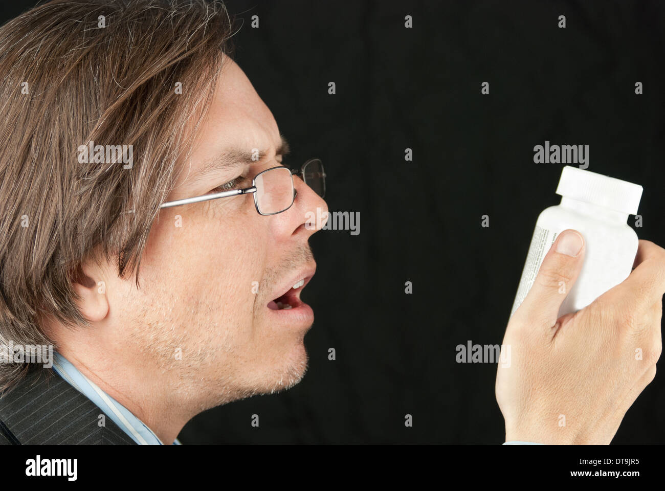 Close-up of a casual businessman wearing glasses trying to read a pill bottle label. Stock Photo