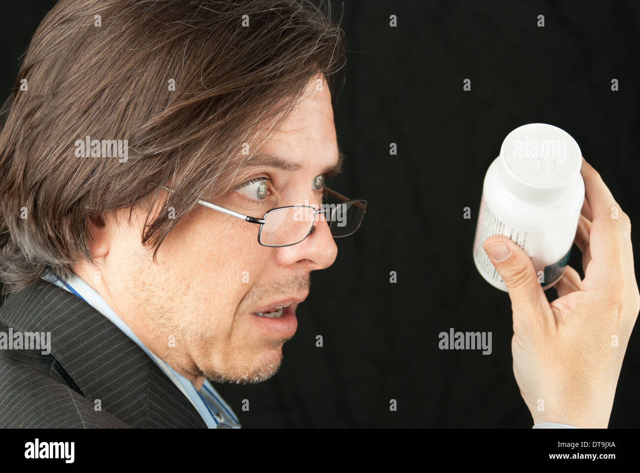 Close-up of a casual businessman looking over glasses trying to read a pill bottle label. Stock Photo