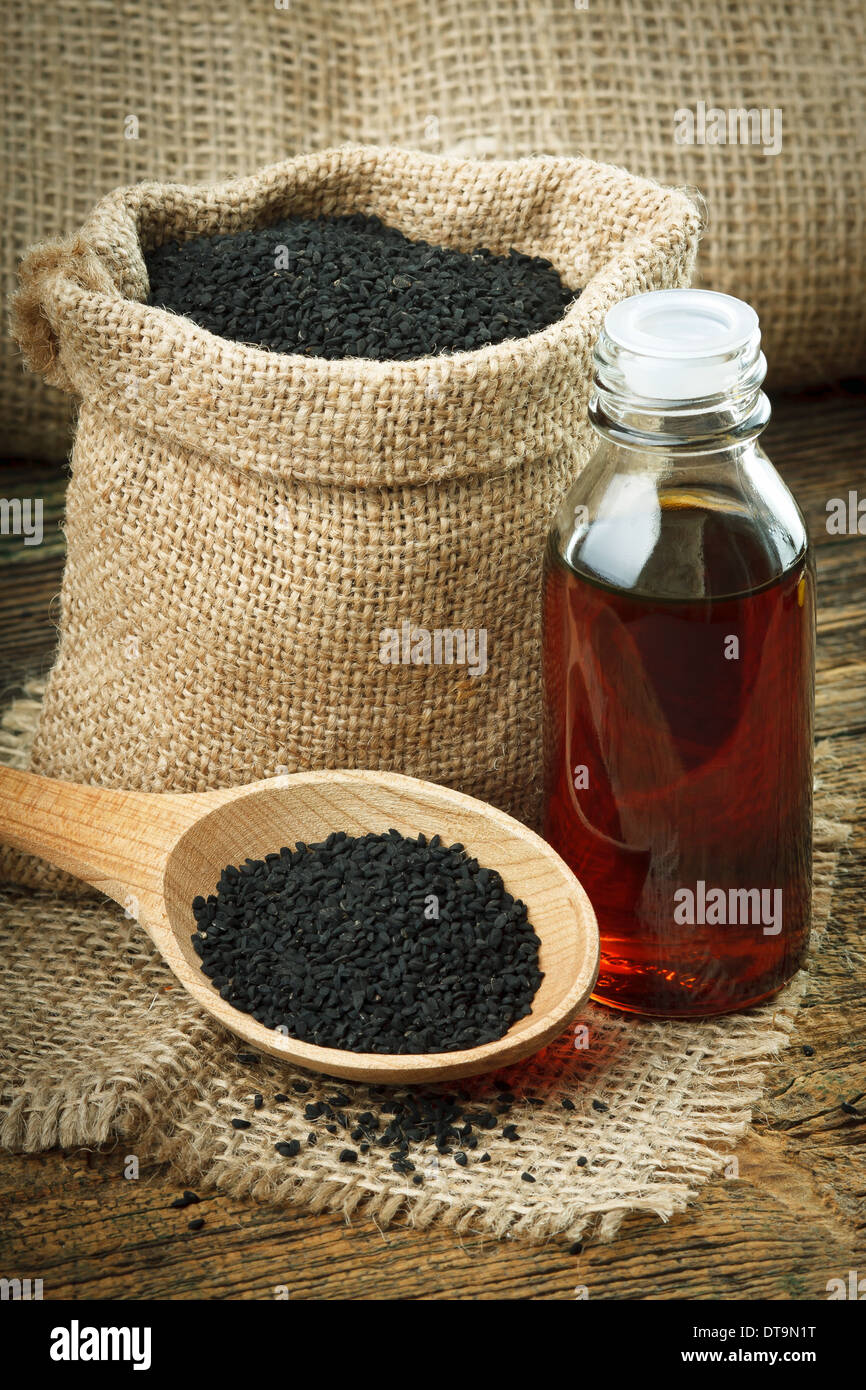Nigella sativa (Black cumin) on wooden spoon and essential oil. Real oil from nigella looks like dark honey Stock Photo