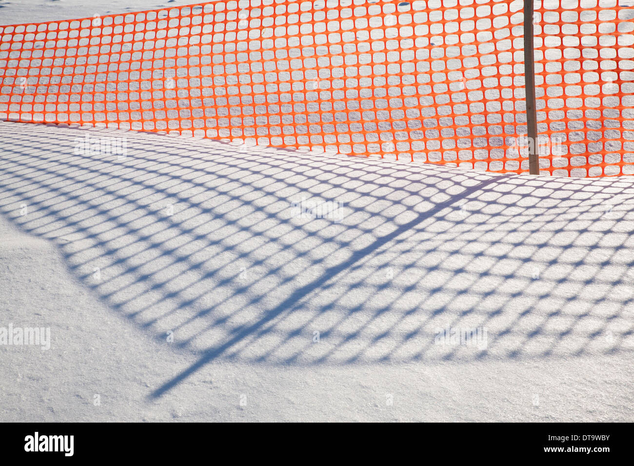 Shadows from an orange plastic snow fence make patterns on the New England snow. Stock Photo