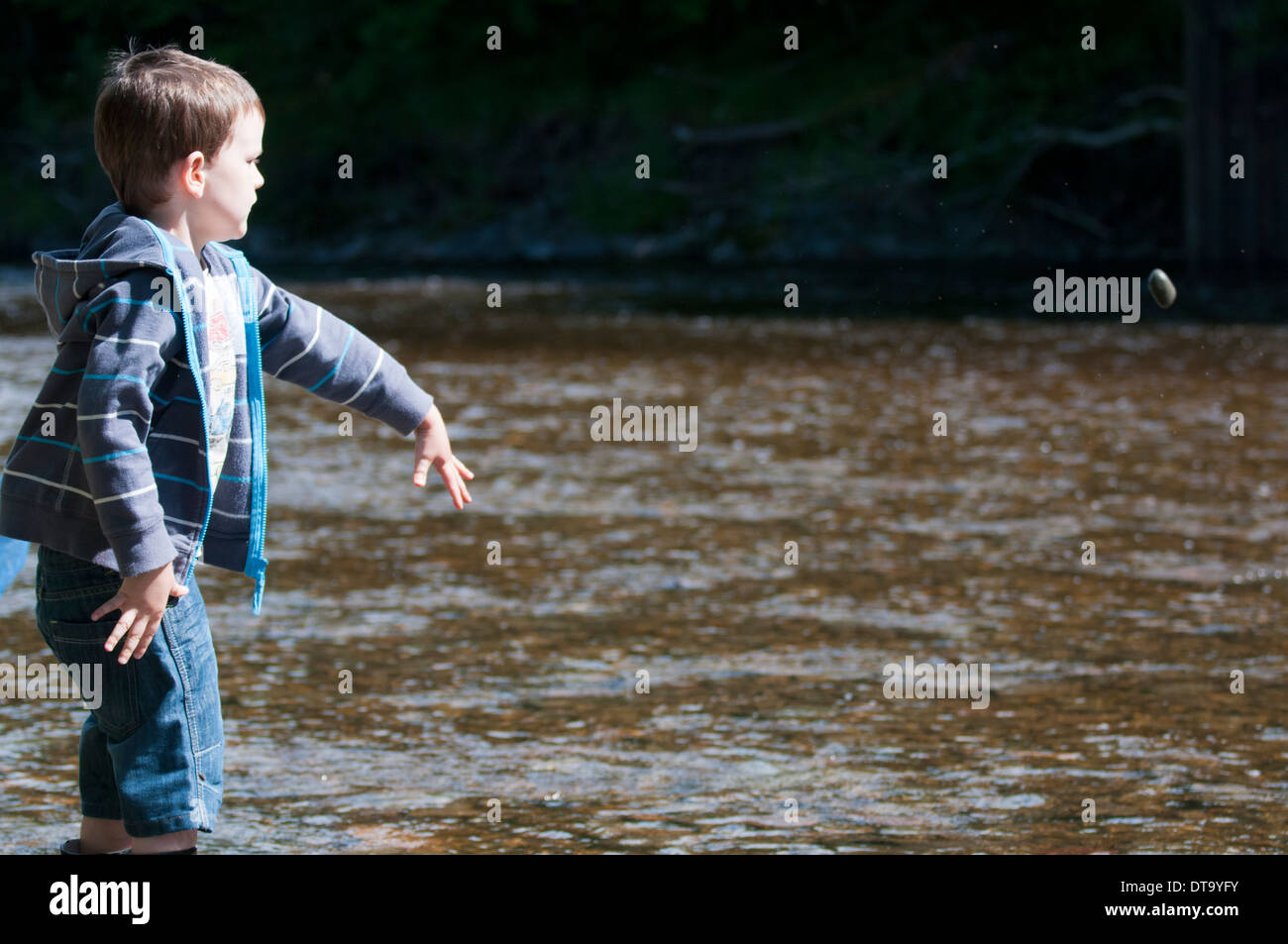 Boy throwing stone into river Stock Photo