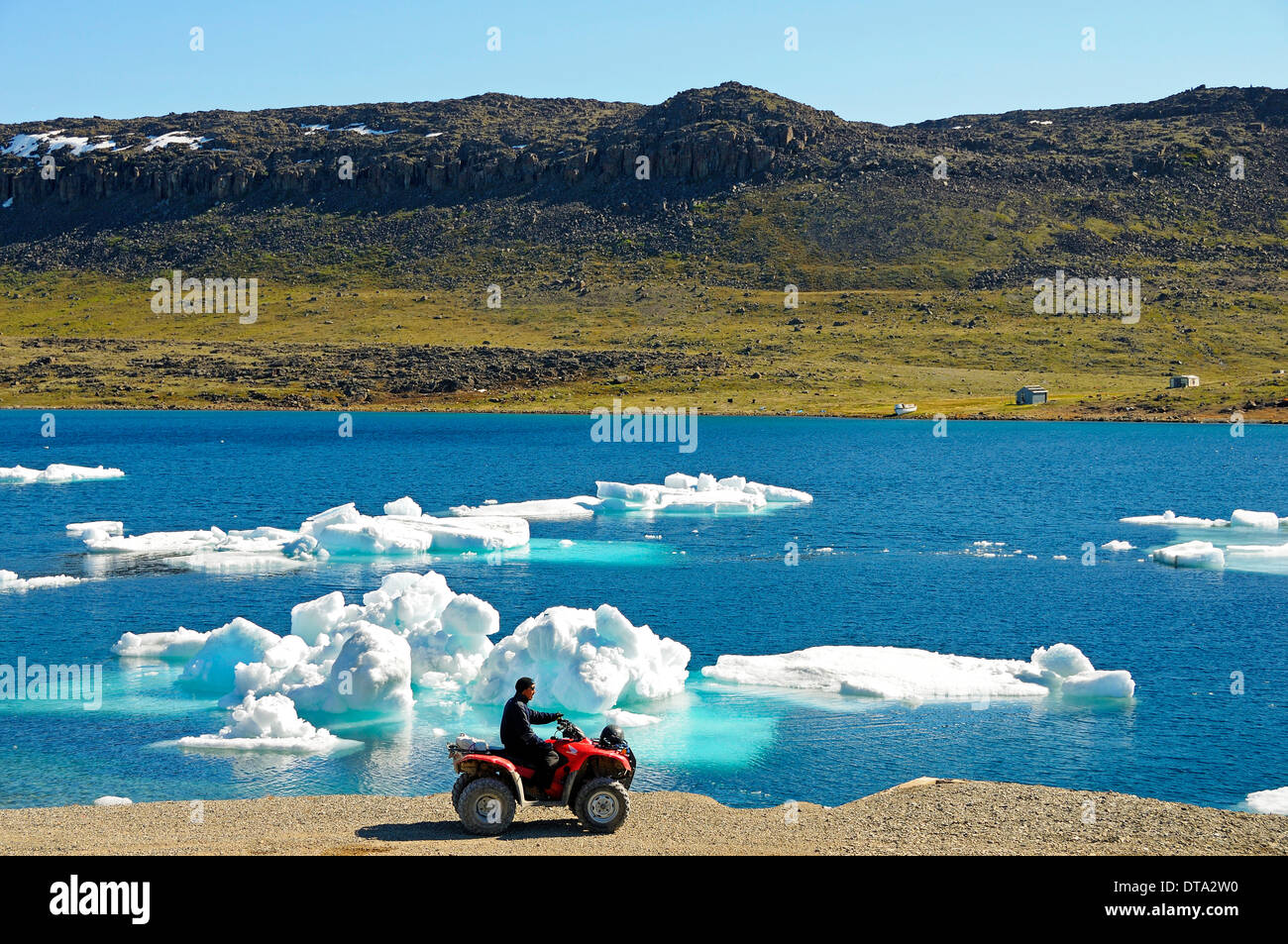 Man of the Inuit people riding a quad bike, ATM, parked on the shore of the Beaufort Sea, Arctic Ocean, Victoria Island Stock Photo