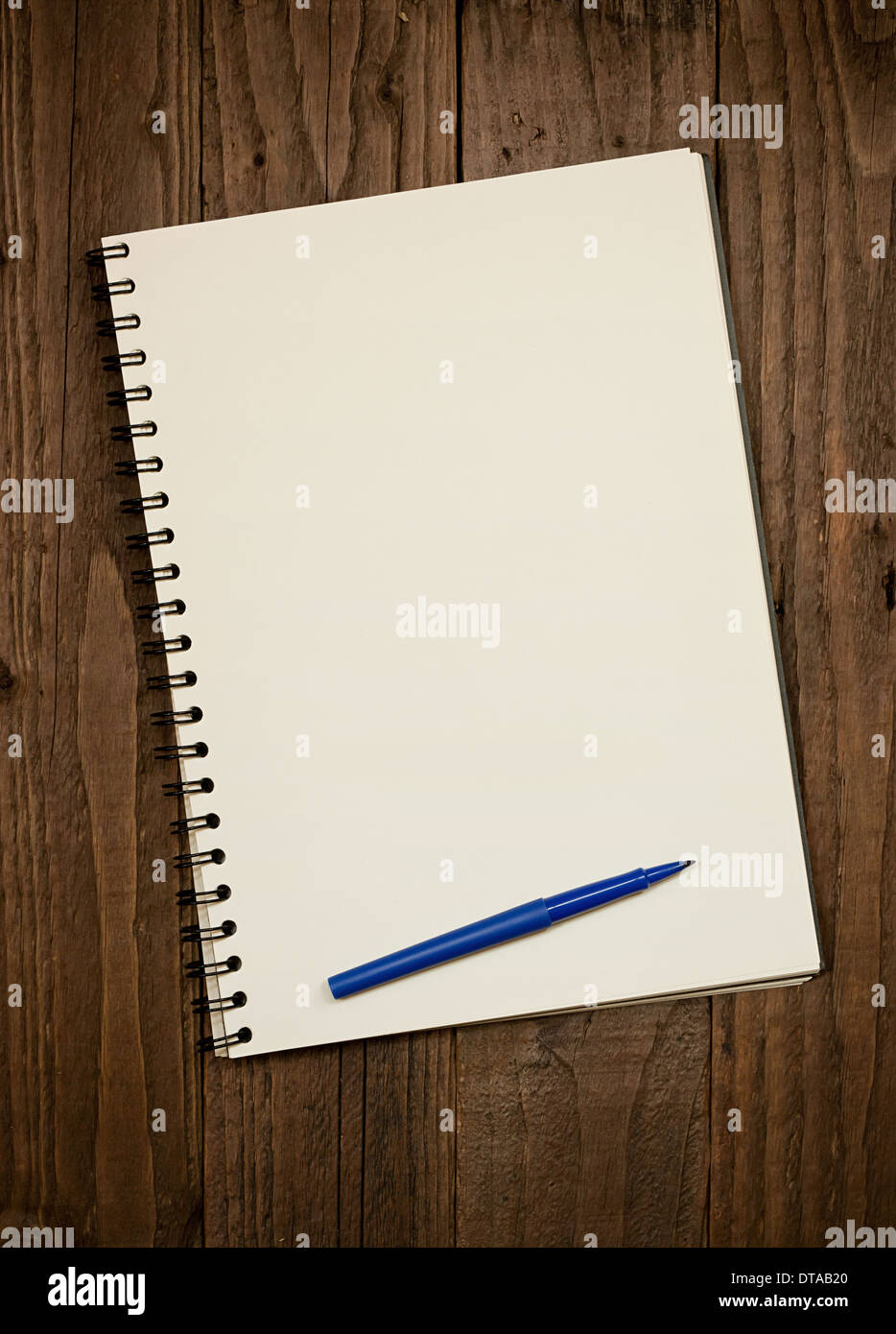 Blank spiral bound scrapbook on a rustic wooden background with copy space and pen at foot of pad. Stock Photo