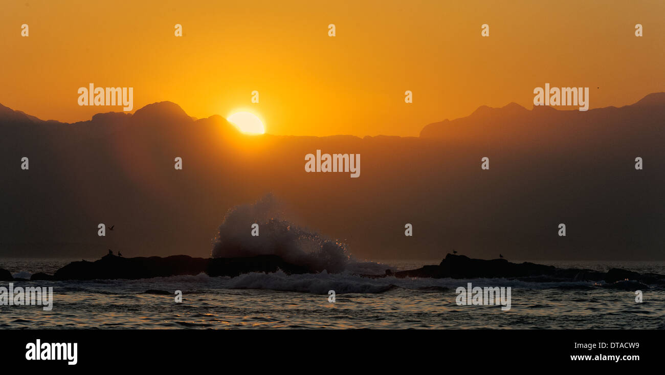 Orange sunrise at the ocean with mountains silhouettes Stock Photo - Alamy