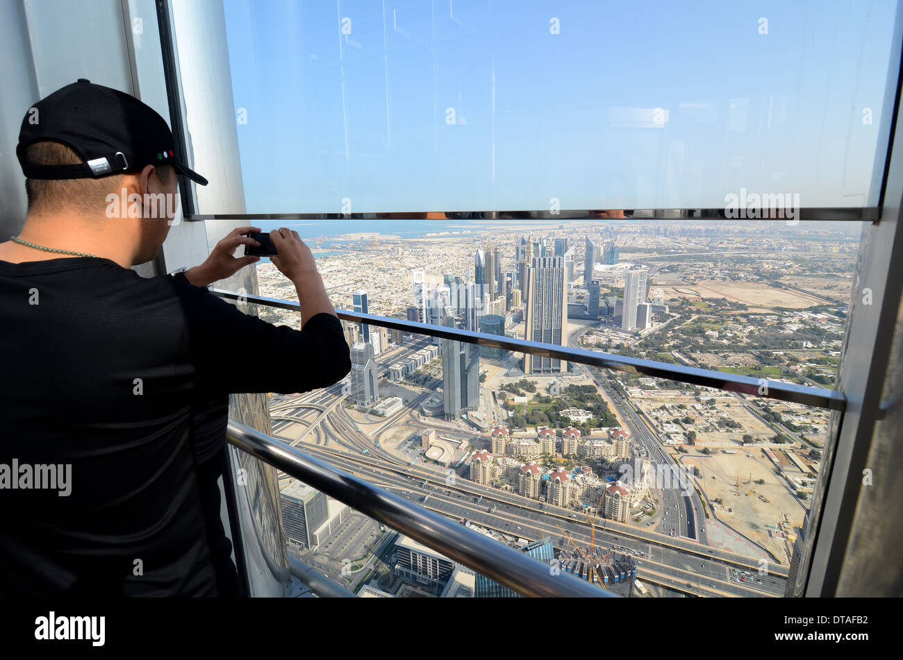 A man taking a photo of central Dubai from the observation deck of the Burj Khalifa, the tallest building in the world. Stock Photo