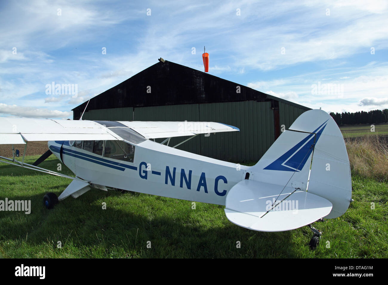 a Piper PA18 Super Cub light aircraft parked outside a hangar with windsock Stock Photo