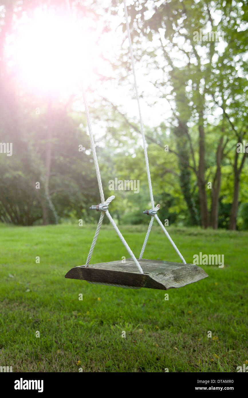 An empty wooden swing in a picturesque garden. Sunlight lens flare. Stock Photo