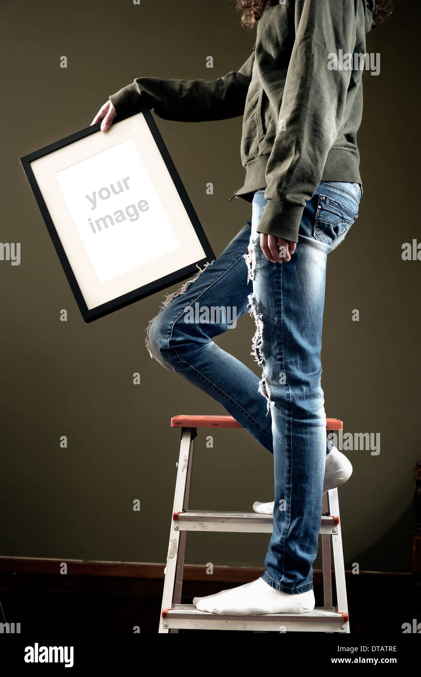 Young female holding picture frame while climbing on a ladder Stock Photo