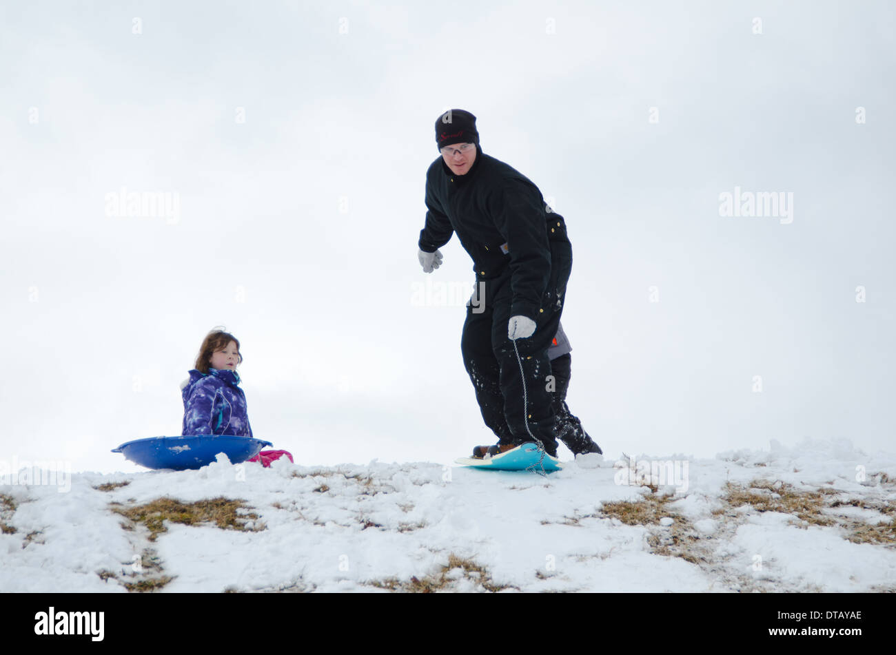 A Daredevil Dad And His Unimpressed Daughter Enjoy A Day Of Sledding On A Rare Snow Day In Knoxville, Tennessee. Stock Photo