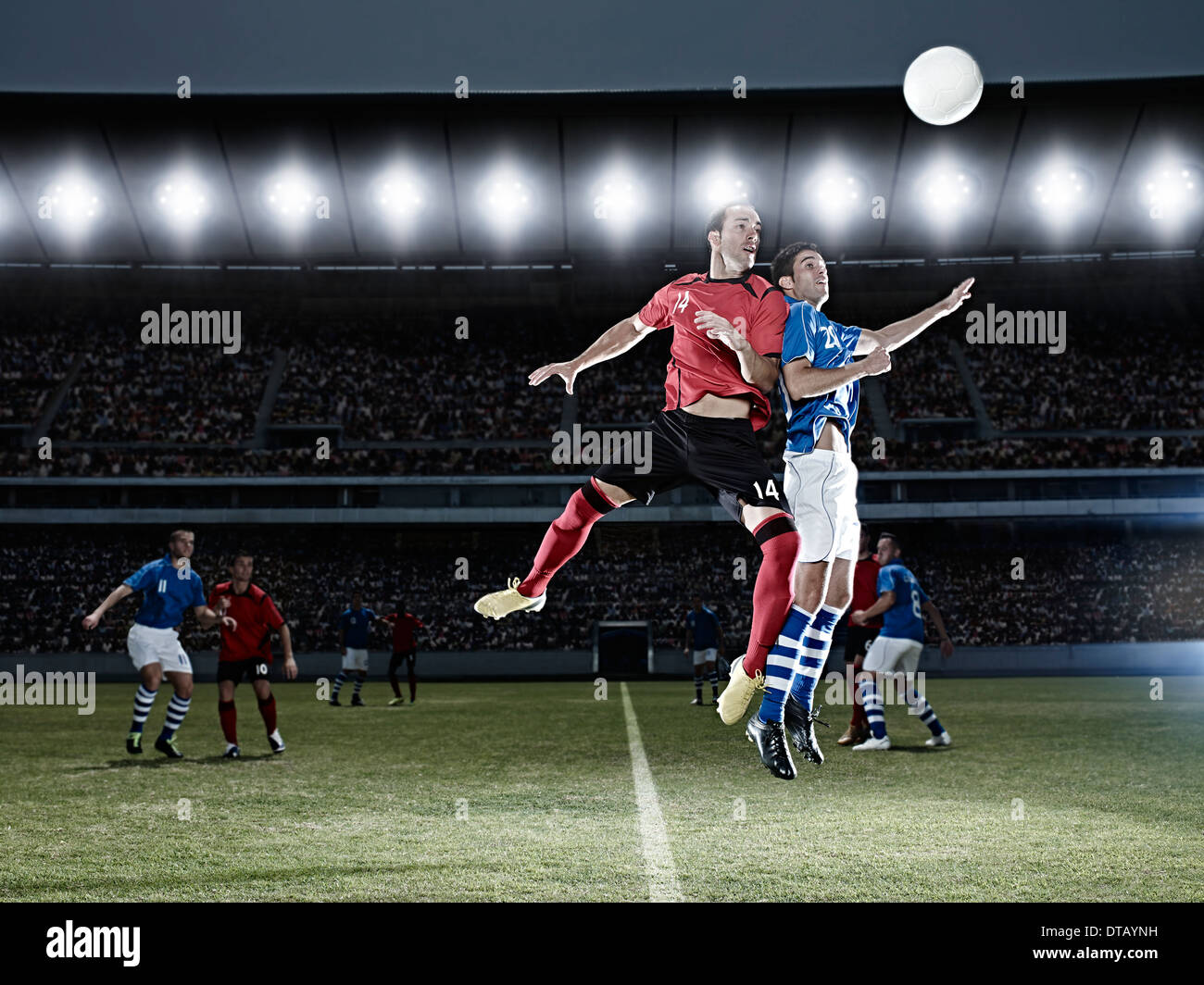 Soccer players jumping for ball on field Stock Photo