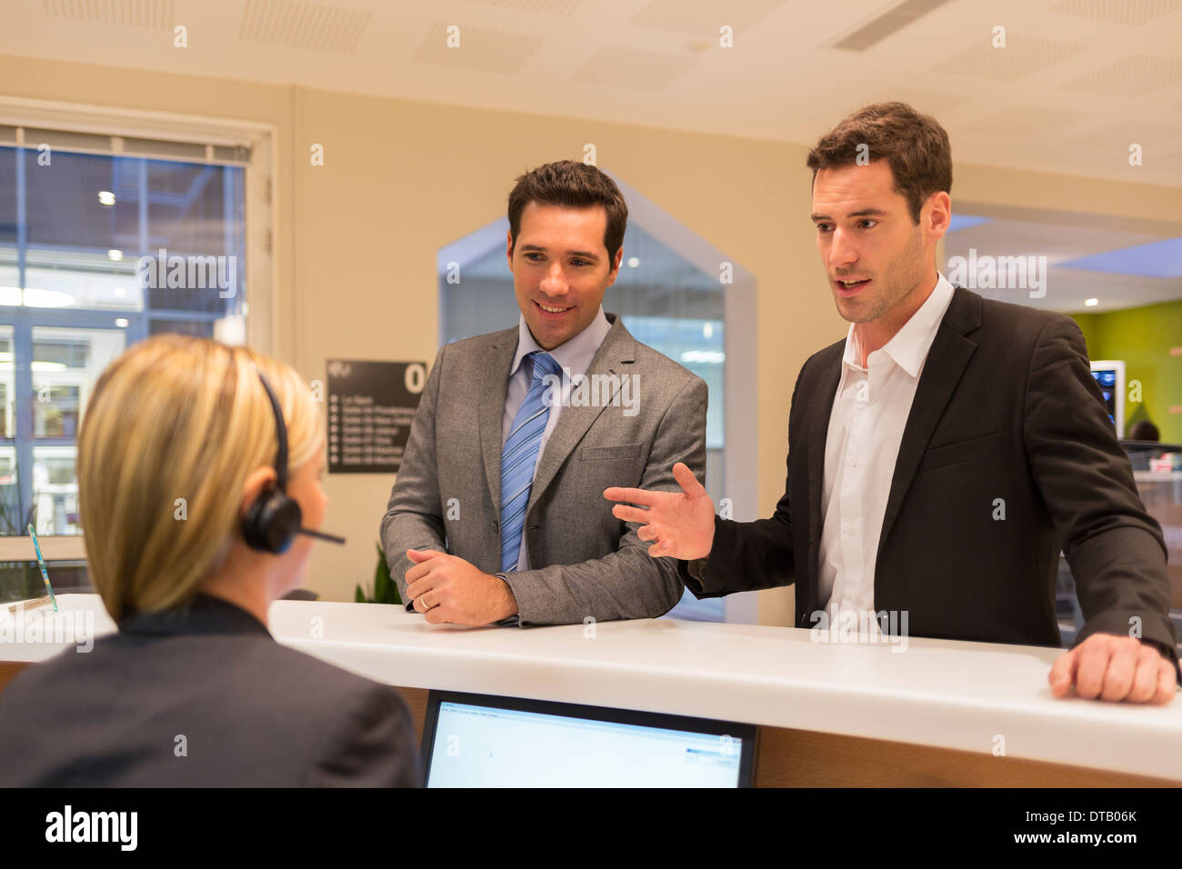 Businessmen communicating with woman receptionist in lobby Stock Photo