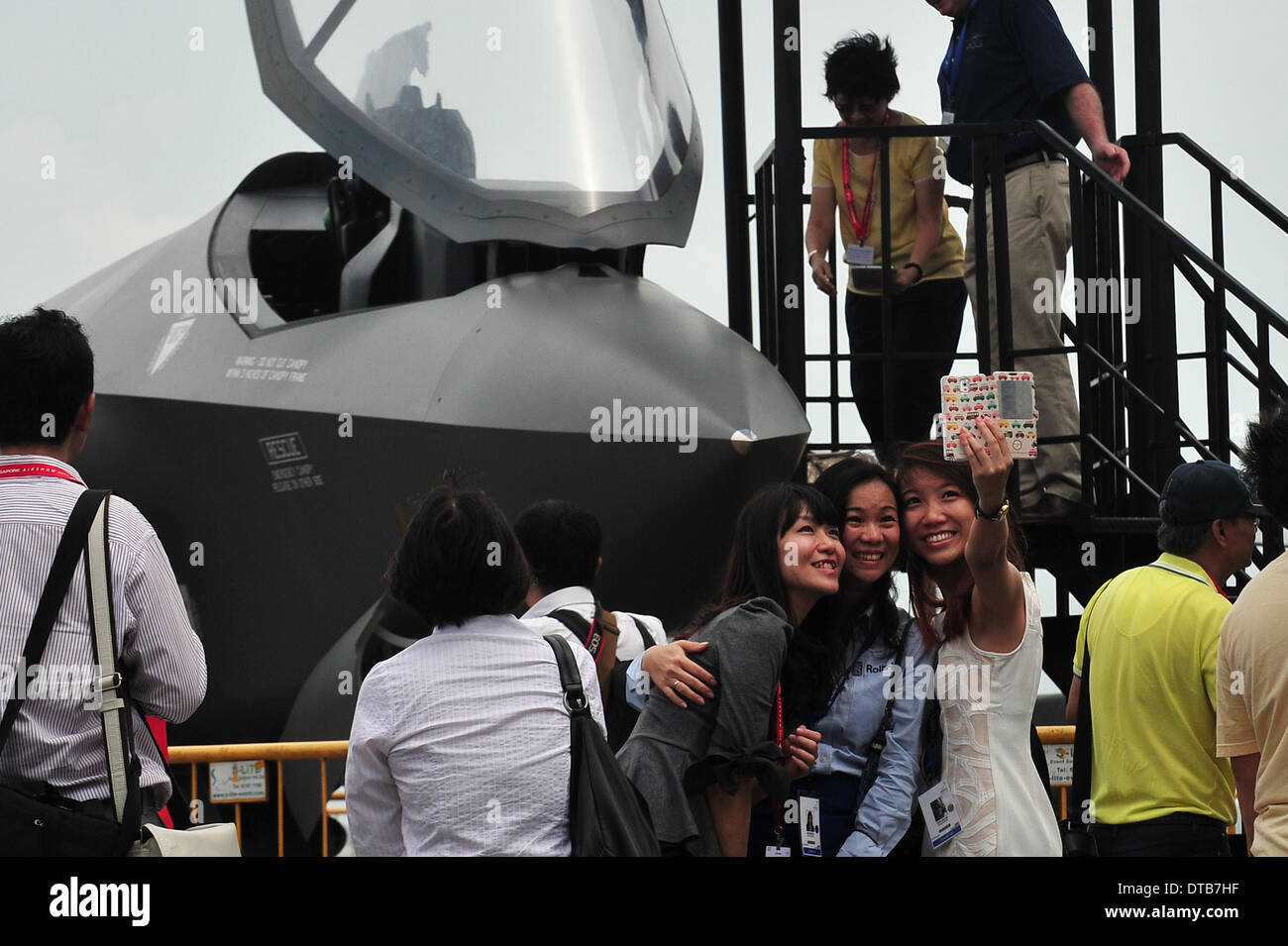 (140214) -- SINGAPORE, Feb. 14, 2014. (Xinhua) -- Three visitors take a picture of themselves with the mock-up of the Lockheed Martin F-35 fighter jet during the Singapore Airshow at Singapore's Changi Exhibition Centre, Feb. 14, 2014. Singapore Airshow entered the last day of the trade show in the Changi Exhibition Centre. (Xinhua/Then Chih Wey) Stock Photo