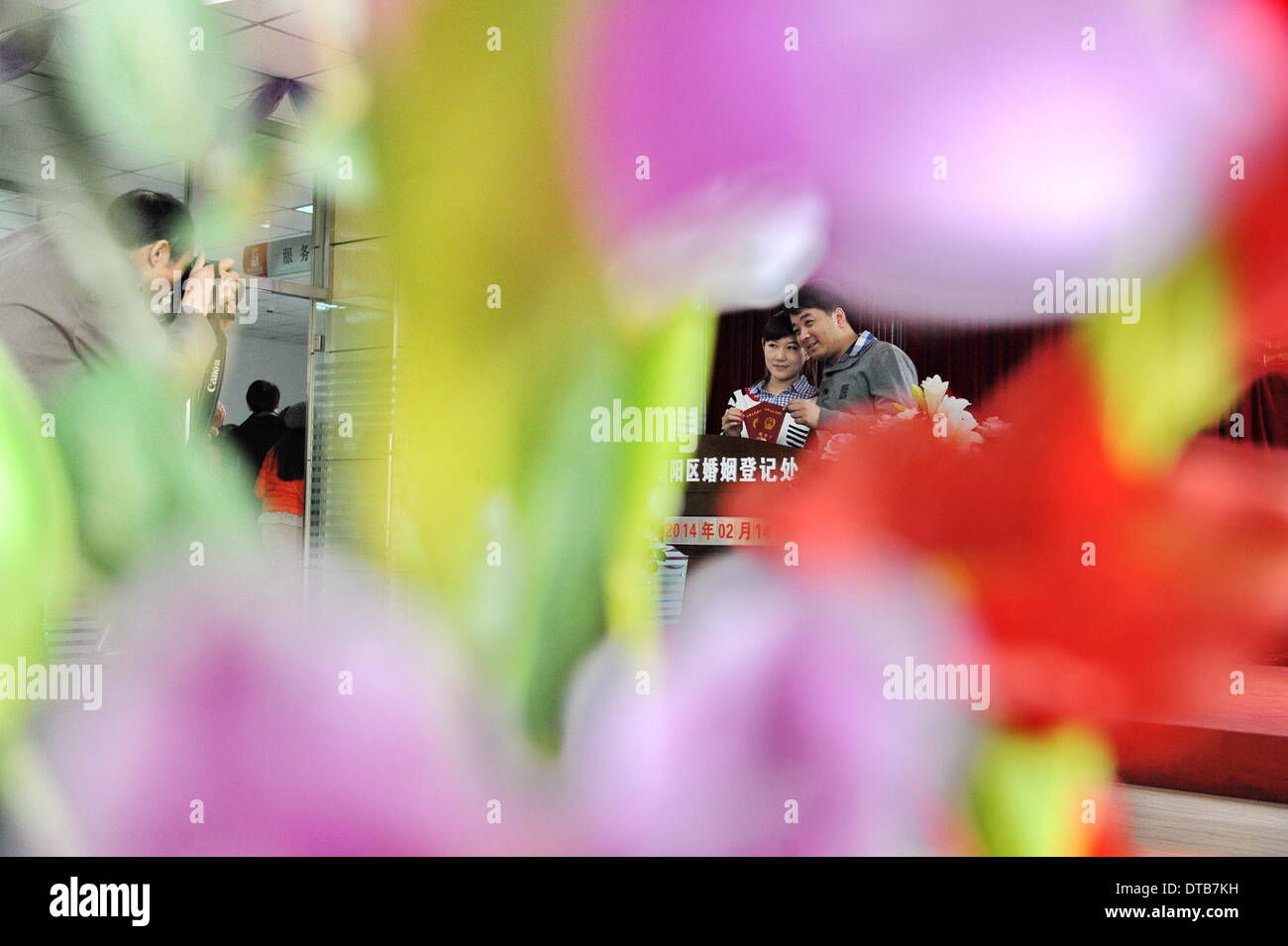 Changchun, China's Jilin Province. 14th Feb, 2014. Newlyweds holding their marriage certificates pose for photos at a marriage registry on the Valentine's Day as well as the Chinese traditional Lantern Festival in Changchun, capital of northeast China's Jilin Province, Feb. 14, 2014. Many newlyweds chose to get marriage licenses on the Valentine's Day this year, as it coincides with the Lantern Festival, the 15th day of the first month of the Chinese lunar calendar. © Zhang Nan/Xinhua/Alamy Live News Stock Photo