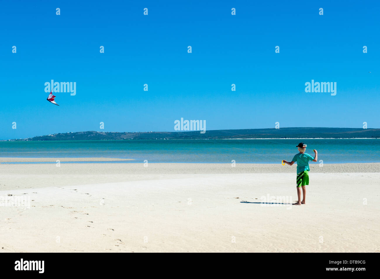 A boy flies his kite on the beach of a lagoon, Churchhaven, Western Cape, South Africa Stock Photo