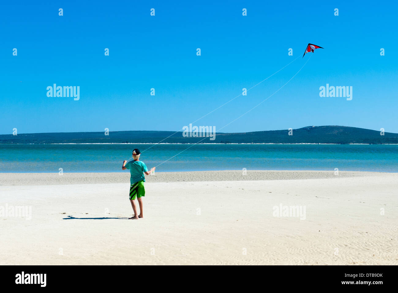 A boy flies his kite on the beach of a lagoon, Churchhaven, Western Cape, South Africa Stock Photo