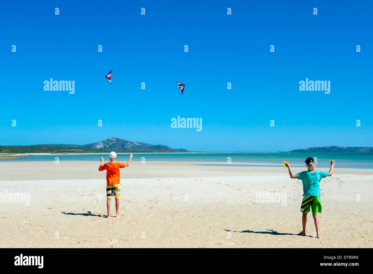 Two boys flying kites on the beach of a lagoon, Churchhaven, Western Cape, South Africa Stock Photo