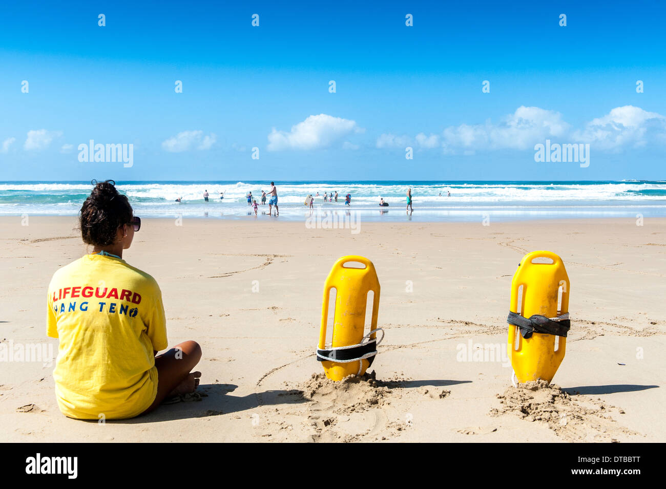 A lifeguard with rescue equipment sitting on the beach watching swimmers in the sea, Sedgefield, Eastern Cape, South Africa Stock Photo