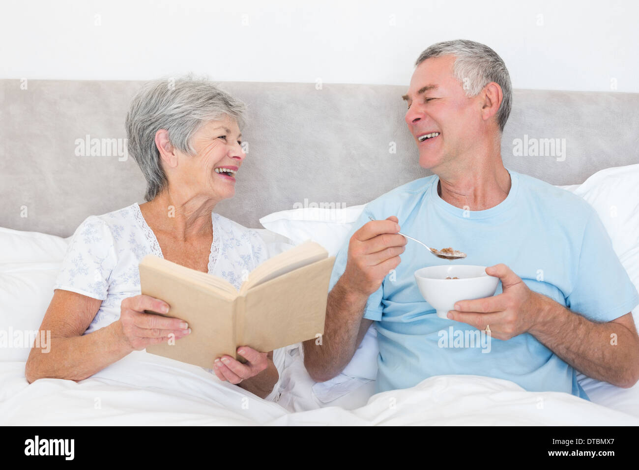 Happy couple with book and bowl in bed Stock Photo