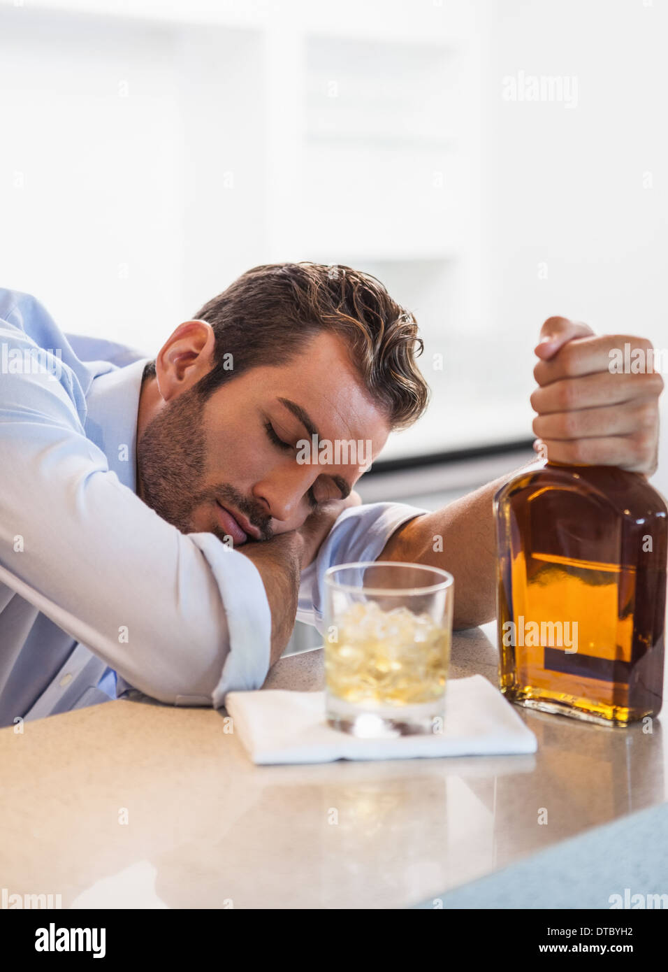 Drunk businessman clutching whiskey bottle asleep Stock Photo