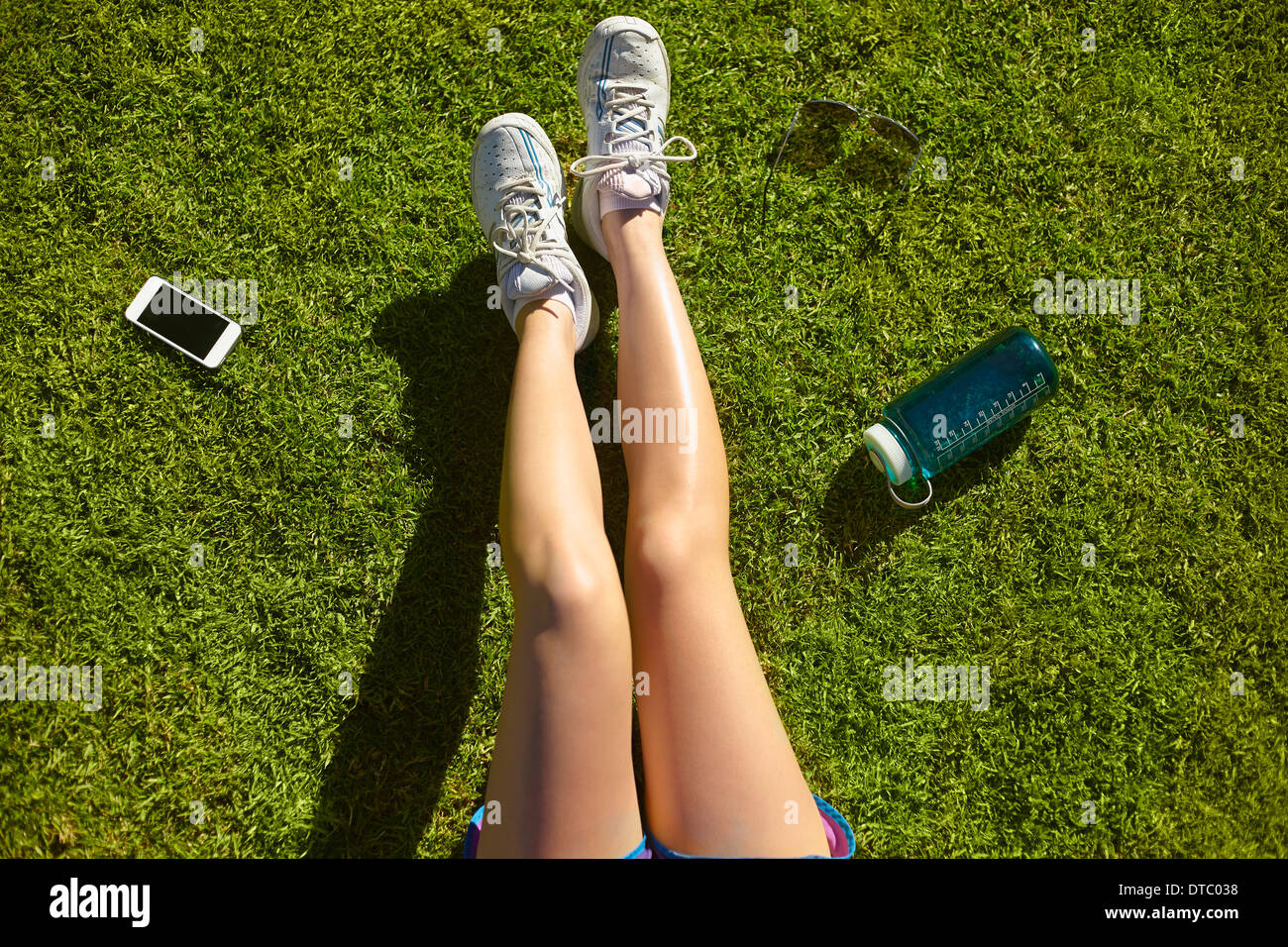 Young woman's legs on sunlit grass in park Stock Photo