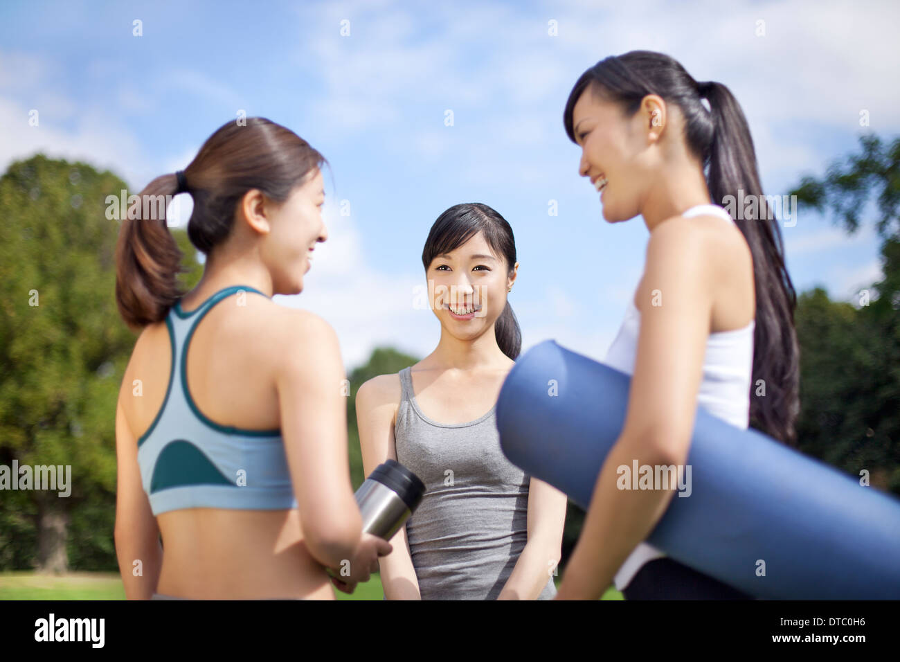 Three young women preparing for yoga practice in park Stock Photo