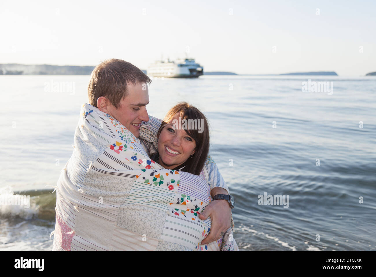 Young couple wrapped in a blanket at coast Stock Photo