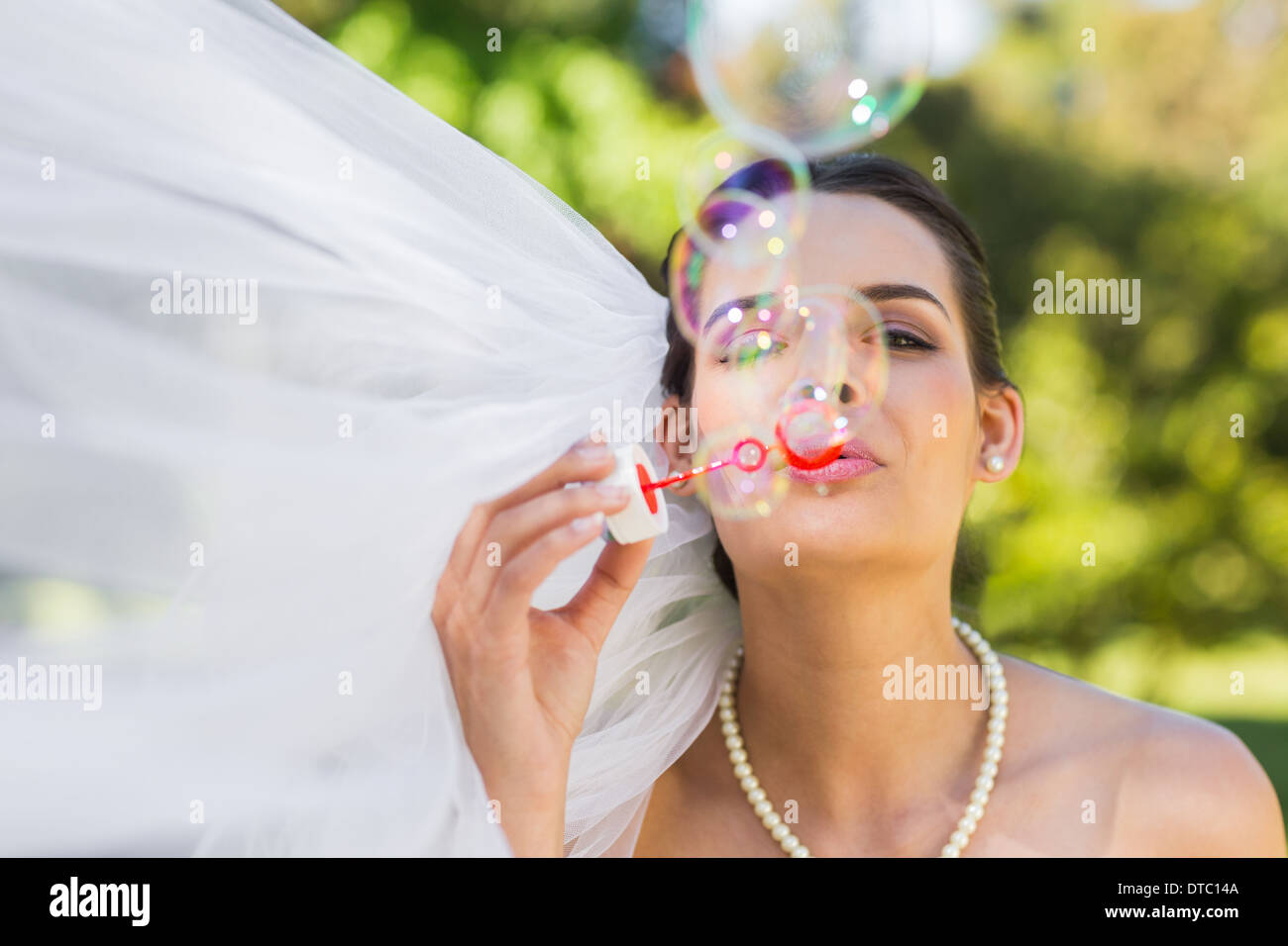Bride blowing soap bubbles in park Stock Photo