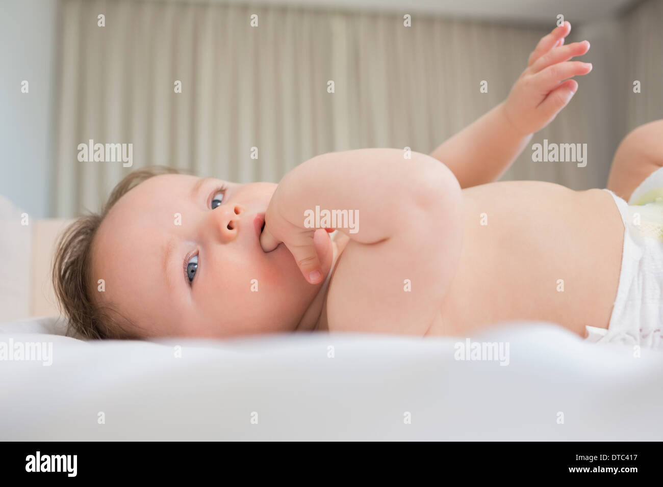 Baby with finger in mouth lying on crib Stock Photo