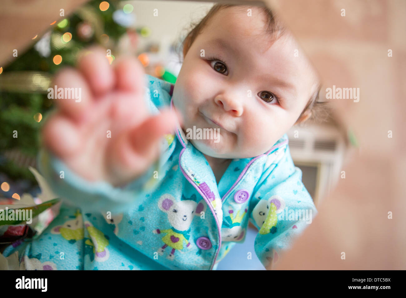 Baby girl wearing pyjamas reaching towards camera Stock Photo