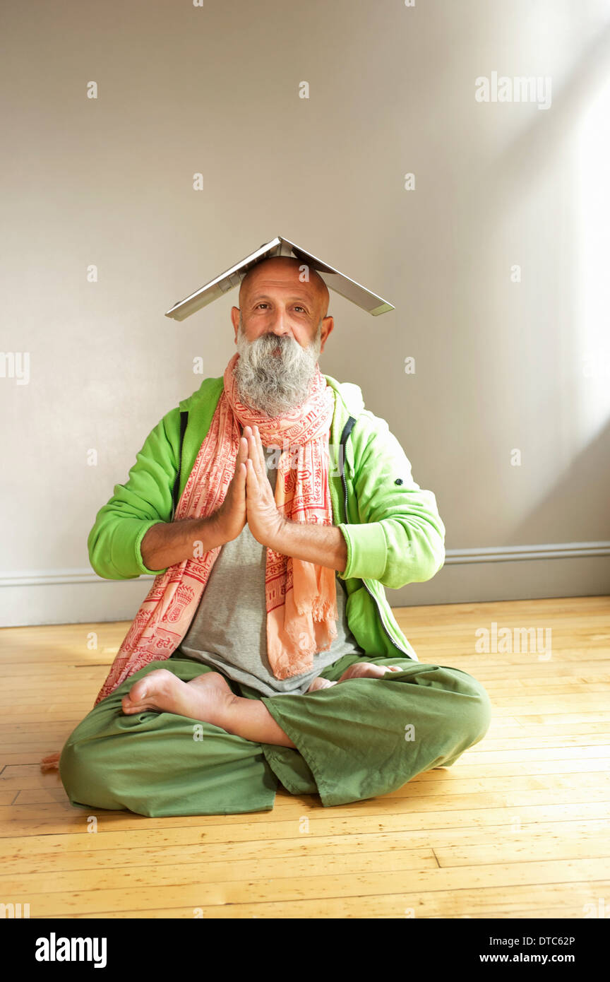 Senior man in lotus position with laptop on head Stock Photo