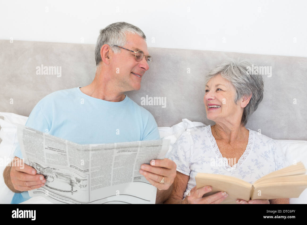 Senior couple with newspaper and book in bed Stock Photo