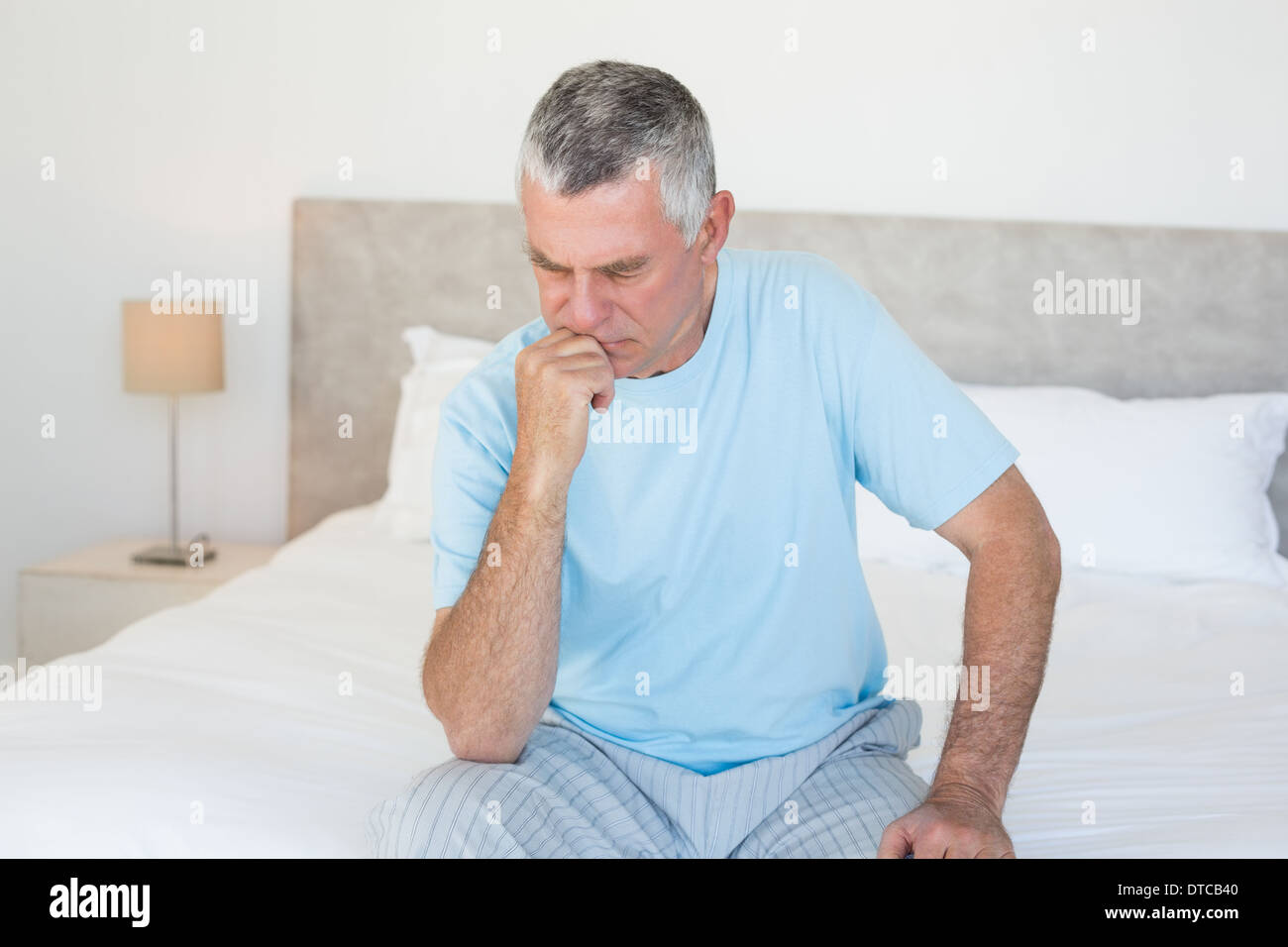 Pensive senior man sitting on bed Stock Photo