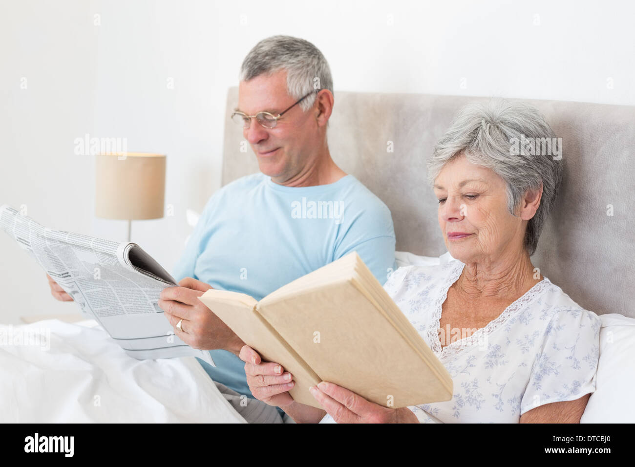 Senior couple reading newspaper and book in bed Stock Photo