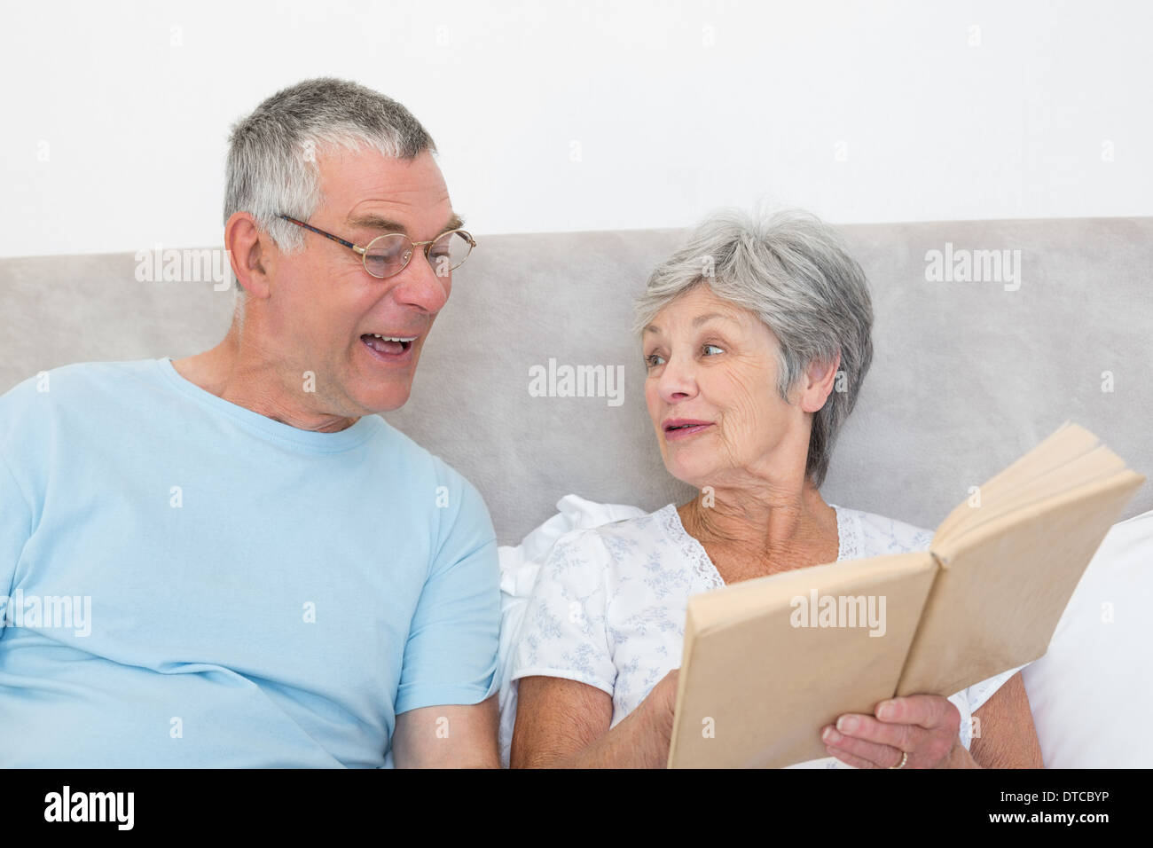 Senior woman showing book to husband in bed Stock Photo