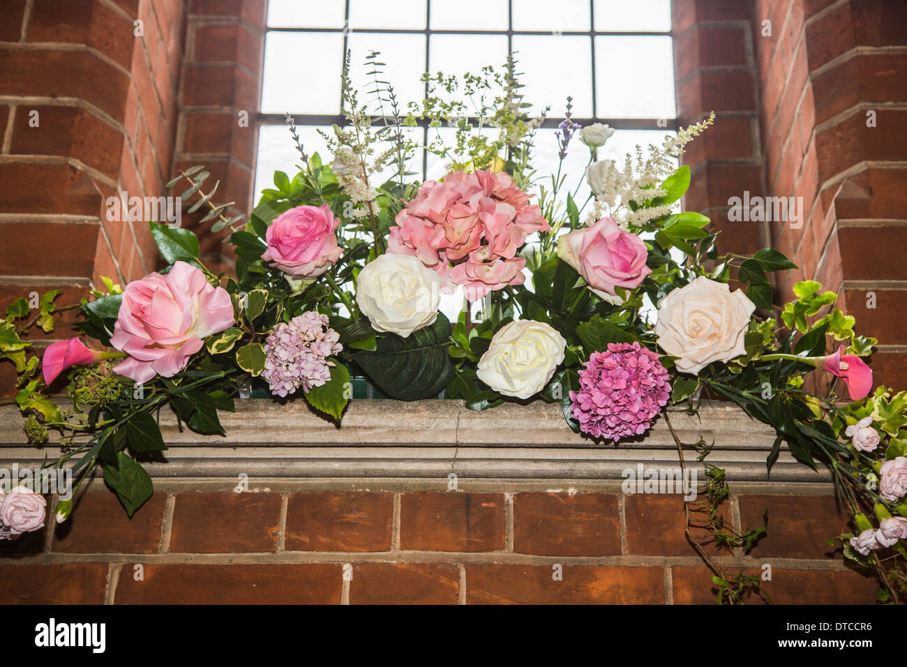 Flower arrangement / floral display with white peonies and green foliage with window and brick wall at Christ Church, Woking Stock Photo