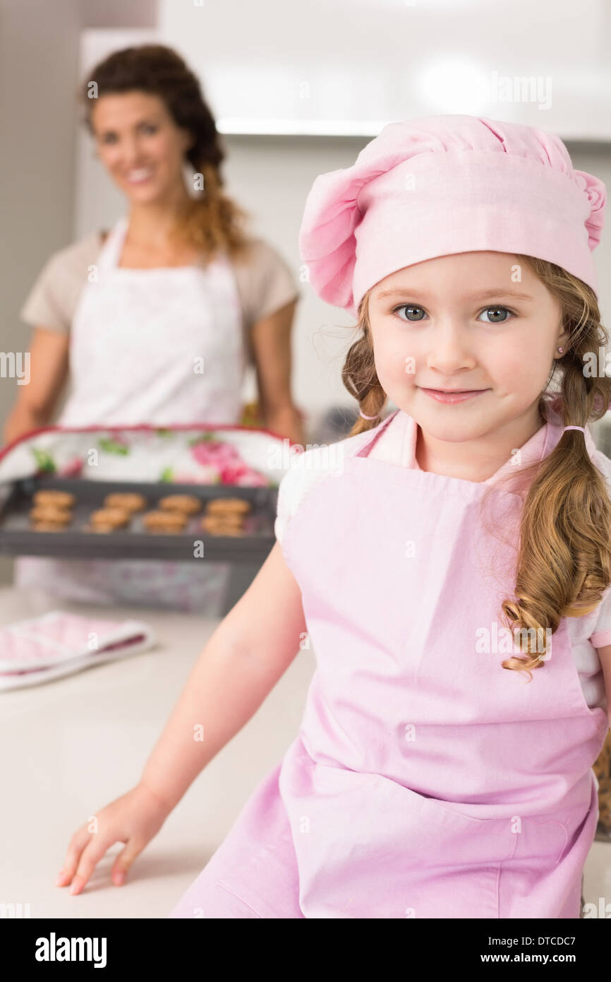 Cute girl wearing pink apron and chefs hat smiling at camera Stock