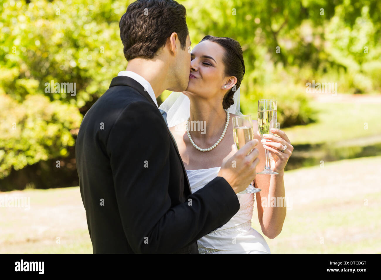 Newlywed kissing while toasting champagne flutes at park Stock Photo