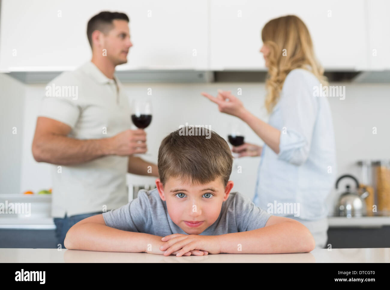 Sad boy leaning on table while parents arguing Stock Photo