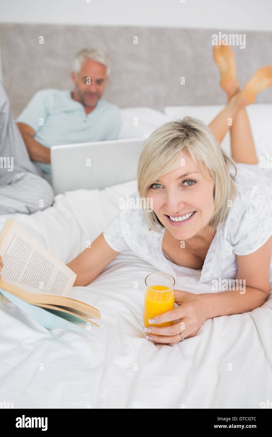 Couple reading book and using laptop in bed Stock Photo